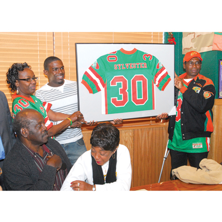 Philip Sylvester holding up his FAMU Venom football jersey surrounded by family members.